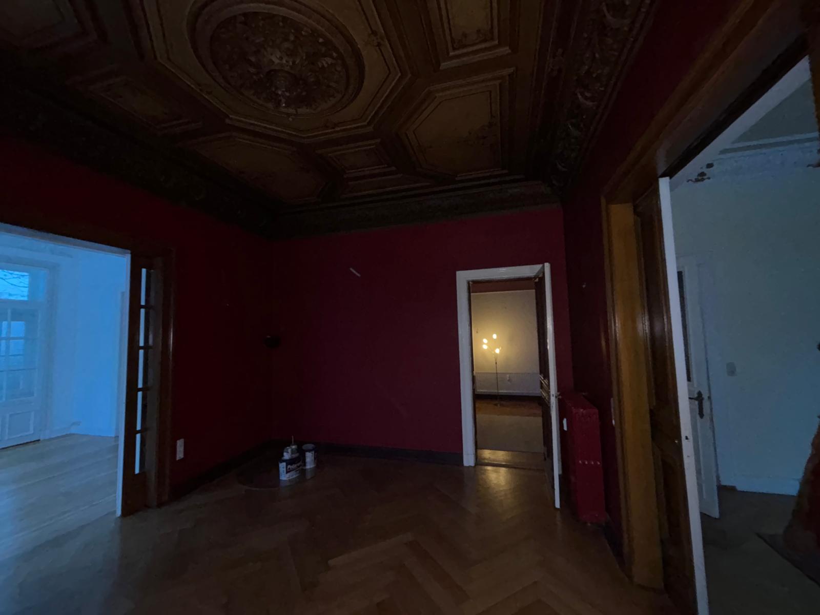 Renovierter Altbau-Raum mit roter Wandfarbe und Stuckdecke